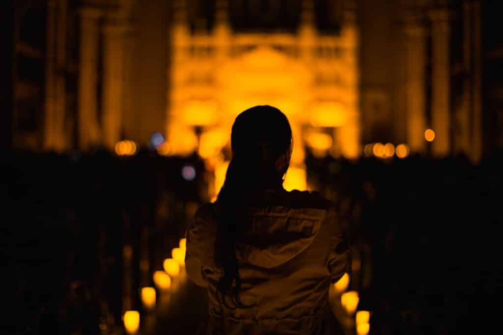 Une femme de dos arrive à un concert Candlelight. On distingue les bougies et le public dans le noir.